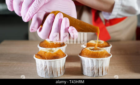 Chef pâtissier comble muffins dans les tasses de papier caramel remplissage avec poche à douille, close-up. Banque D'Images