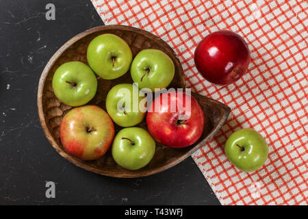 Vue d'en haut, vert et rouge brillant pommes sur bol en bois sculpté, nappe vichy rouge foncé et en conseil en application. Banque D'Images