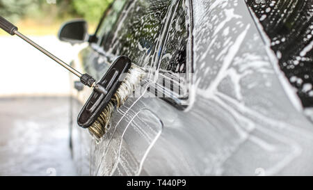 Côté de l'argent un architecte en self service carwash, détails sur le passage de la brosse, shampooing blanc soleil trouble allumé d'arbres en arrière-plan Banque D'Images