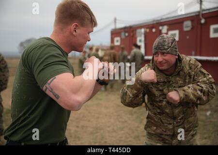 Un U.S. Marine avec des Groupe Force-Crisis Response-Africa air-sol marin 19.1, Forces maritimes de l'Europe et l'Afrique, montre militaire Marine Corps techniques Programme d'Arts Martiaux à un soldat de l'armée géorgienne avec l'infanterie du 12e Bataillon pendant 19,1 Platinum Eagle, un exercice d'entraînement multilatéral tenu au secteur d'entraînement Babadag, en Roumanie, le 16 mars 2019. SPMAGTF-CR-AF est déployée pour effectuer d'intervention en cas de crise et le théâtre des opérations de la sécurité en Afrique et de promouvoir la stabilité régionale en effectuant des exercices de formation militaire dans toute l'Europe et l'Afrique. Banque D'Images