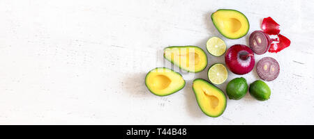 Les moitiés d'avocat, les limes et les oignons - guacamole ingrédients sur conseil de travail blanc, télévision lay photo, grande bannière avec emplacement pour un texte côté gauche Banque D'Images