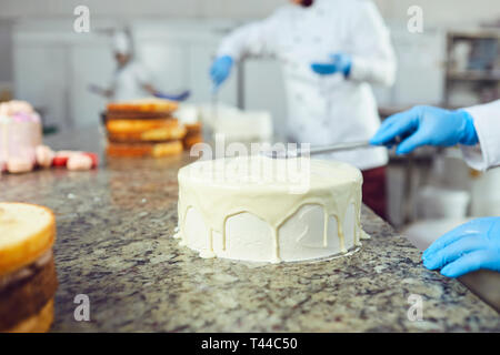 Mains crème confiseur s'étend sur un gâteau blanc sur la table dans la pâtisserie Banque D'Images