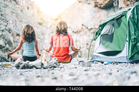 Jeune couple santé faisant du yoga en regard de feu en camping avec tente sur une montagne - Amis méditer sur les roches au coucher du soleil Banque D'Images