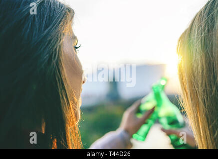 Les jeunes femmes toasting beer sur un coucher du soleil - Happy friends drinking beers et acclamer dans un parc, piscine en plein air en admirant la belle vue Banque D'Images