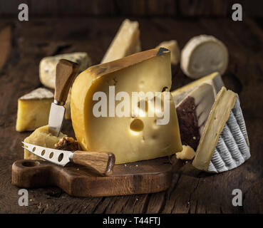 Morceau de fromage Maasdam du lait de vache sur planche de bois. Gamme de fromages à l'arrière-plan. Banque D'Images