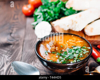 Cuisine géorgienne traditionnelle soupe Kharcho-avec de la viande, le riz et la coriandre fraîche. Soupe épicée Kharcho sur table en bois avec du pain traditionnel Shotis Puri et légumes. Focus sélectif. L'espace de copie pour le texte Banque D'Images