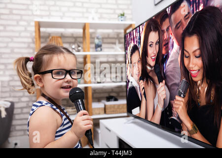 Close-up of a Happy Girl Singing chanson avec micro en face de la télévision à la maison Banque D'Images