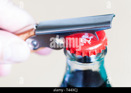 Moscou, Russie - le 4 avril 2019 : l'ouverture d'un bouchon de bouteille en verre de Coca-Cola par ouvre-bouteille close up. Coca-Cola (coke) est raccord spécifique fabriquant de boissons gazeuses Banque D'Images