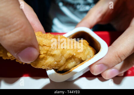 Les mains de l'homme de le consommer le poulet à frire dunks en sauce Banque D'Images