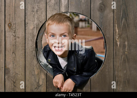 Portrait of happy little boy. le kid est à la recherche de la fenêtre en bois rond et souriant Banque D'Images