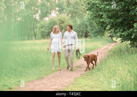 Beau mari et sa femme enceinte avec leur chien sur une promenade dans le parc . photo avec copie espace Banque D'Images