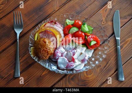 Pomme de terre grillé avec bacon et de tomates, concombres, radis sur le plat en verre avec fourchette et couteau sur la table en bois, vue du dessus Banque D'Images