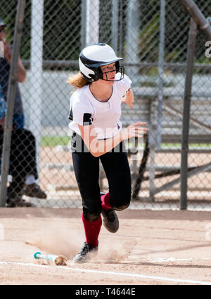 L'école secondaire aux cheveux rouges bousculant softball de la première ligne de base après avoir frappé la balle. Banque D'Images