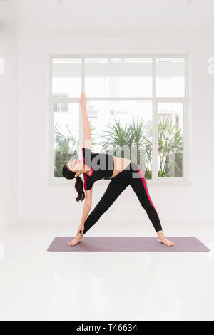 Young attractive woman practicing yoga, debout dans l'exercice, deux guerriers portant des vêtements de sport, piscine pleine fenêtre près de longueur Banque D'Images