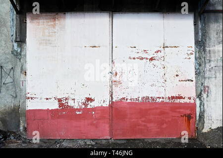 De couleur rouge et blanc entrée old rusty metal gate, représenté à la ville d'Iloilo, aux Philippines, dans la journée. Situé à l'arrière de la porte est une entité industrielle. Banque D'Images