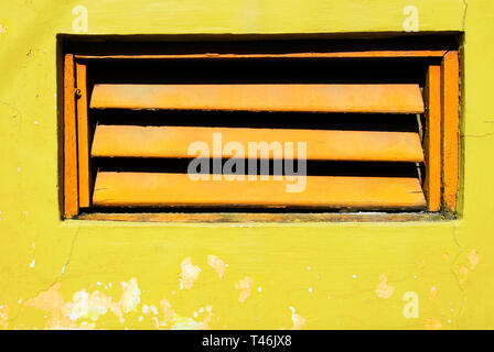 Close-up des volets de couleur orange dans un mur peint en jaune vif avec des ombres Banque D'Images