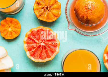 Close up of tropical agrumes avec le jus dans le verre et presse-agrumes sur fond bleu, vue d'en haut. Mise à plat. Mode de vie sain Banque D'Images