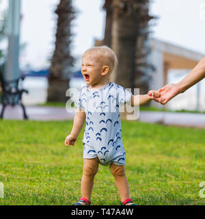 Un petit garçon se dresse sur le fond de l'herbe vert vif et tient sa mother's hands grimace. Banque D'Images