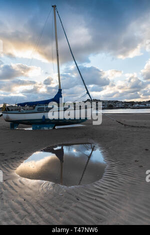 Bateau à voile sur le sable au coucher du soleil, partiellement reflétée dans la flaque. Banque D'Images