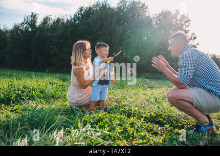 Mère, père et petit fils soufflant des bulles de savon dans la journée d'été. Banque D'Images