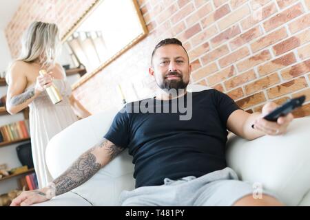 L'homme en regardant la télévision assis dans un fauteuil et une femme est à la recherche en miroir dans l'arrière-plan. Banque D'Images