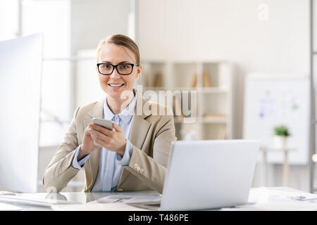 Happy pretty lady texting message tandis que working in office Banque D'Images