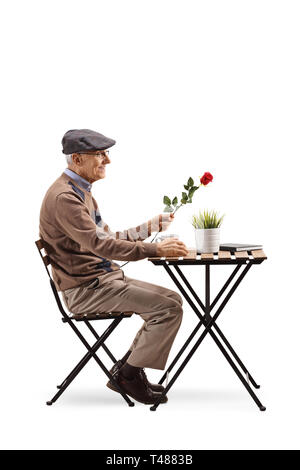 Profil de pleine longueur de balle un homme âgé assis à une table de café et tenant une rose rouge isolé sur fond blanc Banque D'Images
