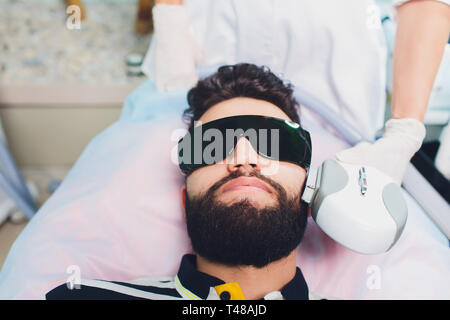 Jeune homme recevant un traitement d'enlèvement de cheveux de laser au centre de beauté. Banque D'Images