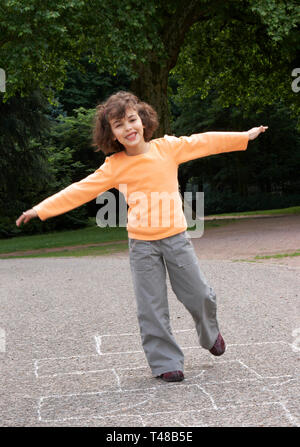 Petite fille jouant à la marelle dans le parc local Banque D'Images