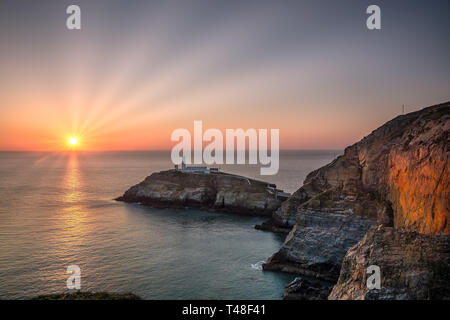 Coucher de soleil spectaculaire à l'horizon, vue sur la mer vers South Stack Lighthouse, Anglesey, au nord du pays de Galles, Royaume-Uni. Banque D'Images