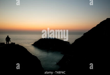 Vue sur phare de South Stack presque comme une silhouette solitaire au crépuscule avec la figure du photographe silhouetté sur colline de prendre des photos en soirée. Banque D'Images