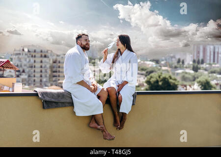 Couple flirter avec vin mousseux sur un toit, s'assoit sur le bord du balcon Banque D'Images