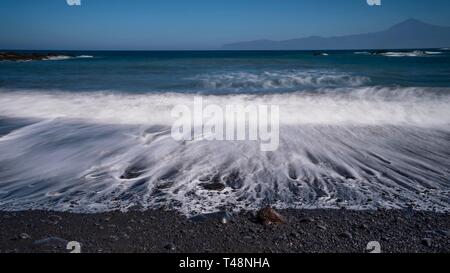 Plage de galets noir avec vague à l'ourlet, temps d'exposition, vue sur le Teide à Tenerife, Playa de Caleta, La Gomera, Canary Islands, Spain Banque D'Images