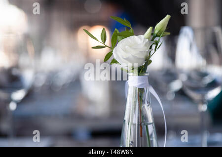 Vase en verre transparent avec bouquet de fleurs contre l'arrière-plan de la table, dans un restaurant moderne. Vin et verres à eau stand dans la rangée de maisons Banque D'Images