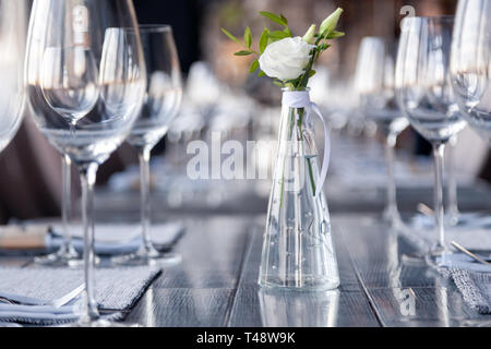 Vase en verre transparent avec bouquet de fleurs contre l'arrière-plan de la table, dans un restaurant moderne. Vin et verres à eau stand dans la rangée de maisons Banque D'Images