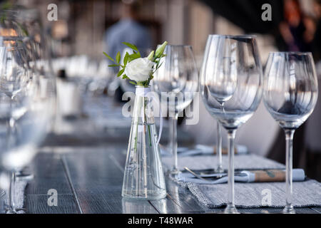 Vase en verre transparent avec bouquet de fleurs contre l'arrière-plan de la table, dans un restaurant moderne. Vin et verres à eau stand dans la rangée de maisons Banque D'Images