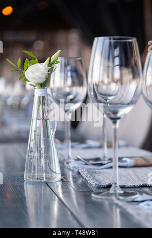 Vase en verre transparent avec bouquet de fleurs contre l'arrière-plan de la table, dans un restaurant moderne. Vin et verres à eau stand dans la rangée de maisons Banque D'Images