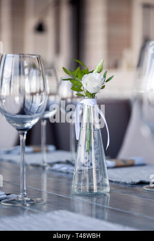 Vase en verre transparent avec bouquet de fleurs contre l'arrière-plan de la table, dans un restaurant moderne. Vin et verres à eau stand dans la rangée de maisons Banque D'Images