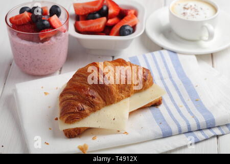 Petit-déjeuner français : croissant sandwich avec du fromage, salade de fruits, graines de chia, yaourt et une tasse de cappiccino Banque D'Images