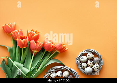 Mise à plat de Pâques sur papier orange avec copie-espace. Oeufs de cailles au nid d'oiseau, printemps tulipes, enveloppe et décorations florales Banque D'Images