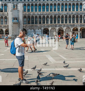 Venise, Italie, 4 septembre 2018. Venise est une ville d'Italie. Les touristes à pied sur la place Saint Marc. Touriste dans un t-shirt blanc tenant un pigeon sur son han Banque D'Images