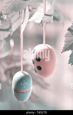Gros plan sur les oeufs de Pâques en bois décoratif suspendu à une branche avec des feuilles au printemps, à l'image filtrée et menthe couleur corail Banque D'Images