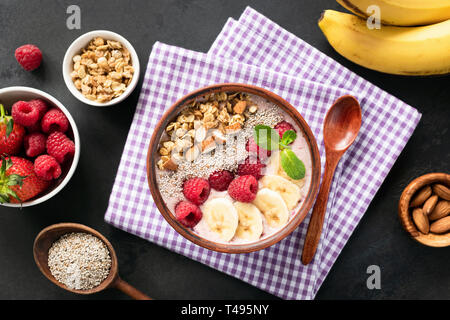 Bol à smoothie Acai baies, fruits, céréales, amandes et noix de coco dans un bol. Arrière-plan de béton noir. Vue d'en haut. Concept d'une saine alimentation, en bonne santé Banque D'Images