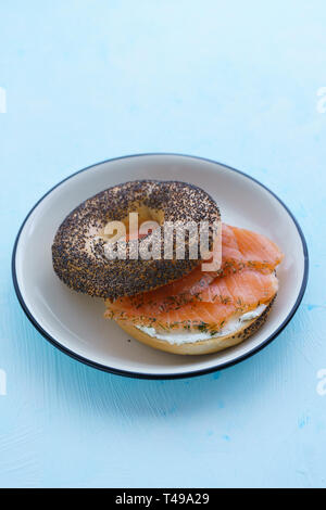 Les graines de pavot bagel avec fromage à la crème et saumon fumé servi sur une plaque blanche avec jante noir. Tableau bleu, haute résolution Banque D'Images