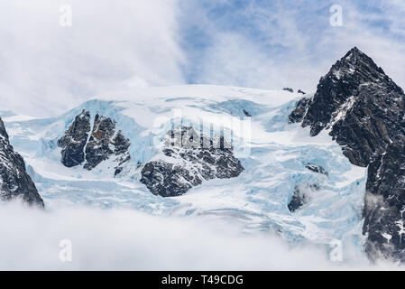 La neige et la glace de glacier couverts rocky mountain peak, avec du brouillard et des nuages blancs ci-dessous dans un ciel bleu au-dessus, Fjord Drygalski, Géorgie du Sud Banque D'Images