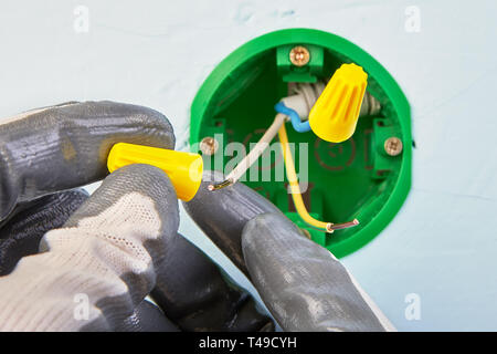 Gants de protection de travailleur est de mettre des conducteurs électriques sur les fils dans le boîtier électrique ronde pour l'interrupteur d'éclairage mural. Banque D'Images