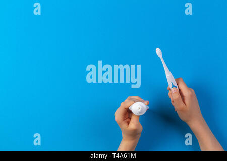 Kid hand holding brosse à dents électrique et mettre coller à partir de tube de dentifrice sur fond bleu Banque D'Images