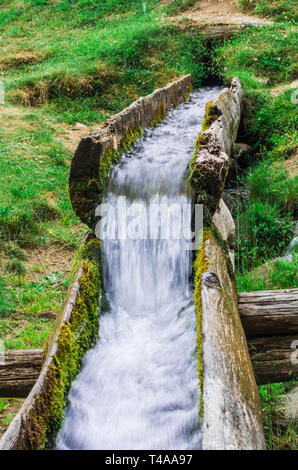 L'eau source de vie coule frais et pur de la montagne vers la vallée dans un canal en bois dans la nature Banque D'Images