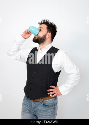Beau jeune homme avec barbe noire posant avec la tasse de café ou thé turquoise tasse in front of white background et décisions différentes expressions du visage Banque D'Images
