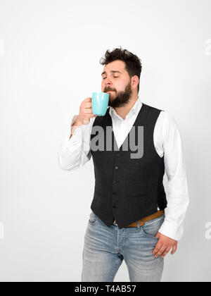 Beau jeune homme avec barbe noire posant avec la tasse de café ou thé turquoise tasse in front of white background et décisions différentes expressions du visage Banque D'Images
